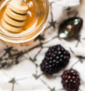 Honey dipper and jar with blackberries on a patterned surface