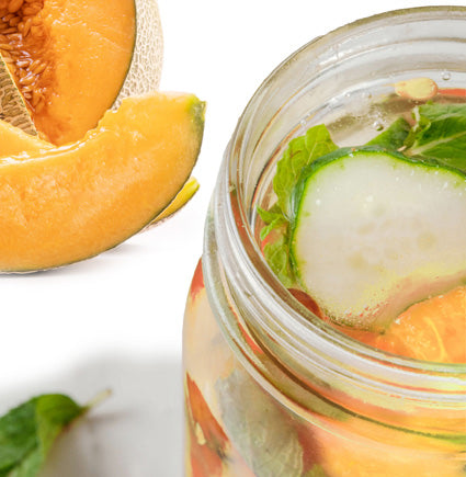 Glass jar with sliced melon and cucumber on a white background